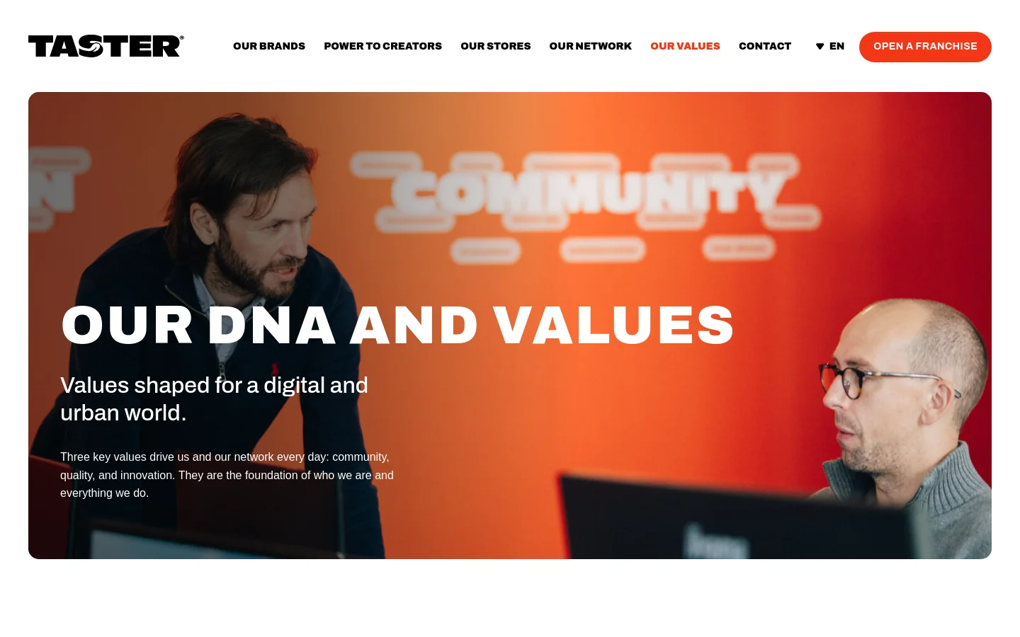 The desktop page features a large hero image with an orange gradient background showing two men, overlaid with the headline 'OUR DNA AND VALUES' and introductory text. A white navigation bar at the top includes the Taster logo, links for Our Brands, Power to Creators, Our Stores, Our Network, Our Values, and Contact, alongside a language selector and a red 'OPEN A FRANCHISE' button. The layout is spacious with clean typography.
