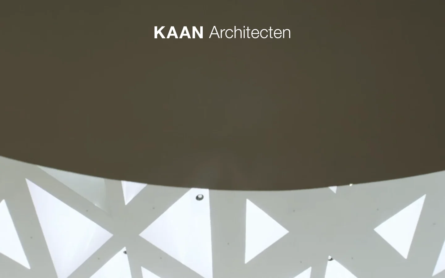 The desktop homepage features a minimalist design with a large, atmospheric hero image of geometric architectural light patterns in white and grey. The 'KAAN Architecten' logo is centered in white text at the top. Below the hero section, the layout transitions to a clean white background with a navigation menu, a grid of project images, and a news section.