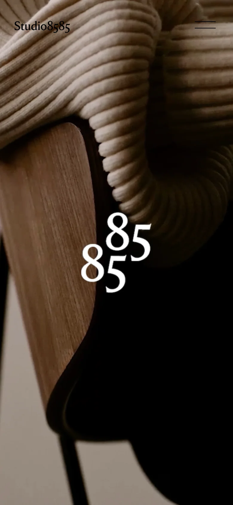 The mobile version maintains the warm-toned hero image of the ribbed sweater and wooden chair. The navigation is condensed, replacing the top-right text links with a hamburger menu icon in the top right, while the studio name remains in the top left.