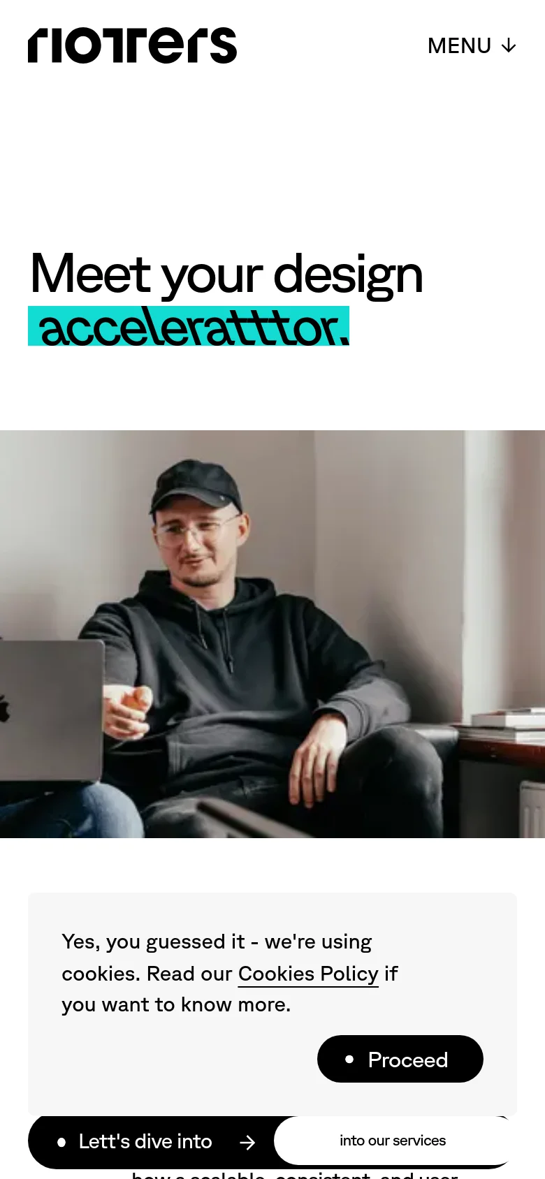 The mobile version presents a vertically stacked layout with the 'Riotters' logo and a 'MENU' dropdown at the top. The headline 'Meet your design acceleratttor.' appears prominently above a large, centered hero image of two men with a laptop. A cookie consent banner with a black 'Proceed' button is visible at the bottom of the screen.