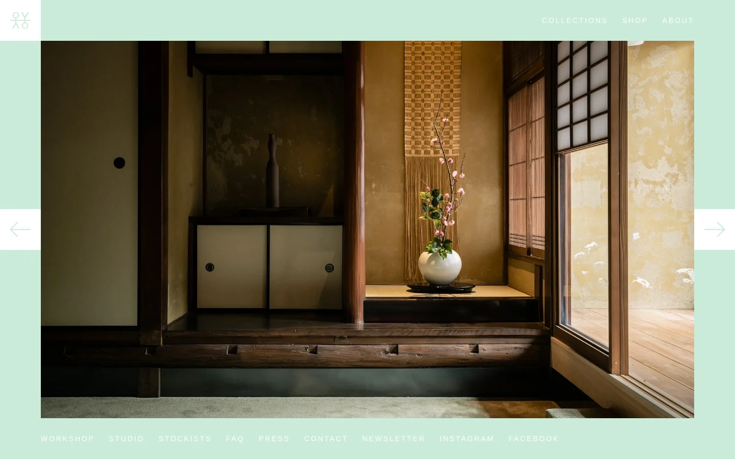 The desktop page features a mint green header and footer with a large, centered hero image of a minimalist Japanese-style interior with dark wood, a floral arrangement in a white vase, and a sliding door. Navigation links for Collections, Shop, and About are in the top right, while a carousel navigation arrow appears on both sides of the image.