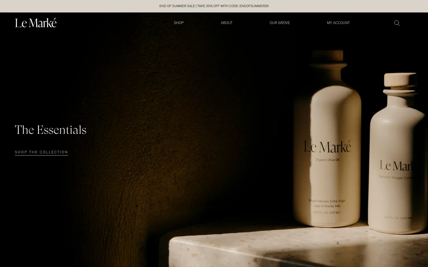 The desktop homepage features a dark, minimalist aesthetic with a large hero image of ceramic olive oil and balsamic vinegar bottles on a stone surface. A navigation menu sits at the top with links for Shop, About, Our Story, and My Account, while the headline 'The Essentials' and a 'Shop the Collection' call to action are positioned on the left.