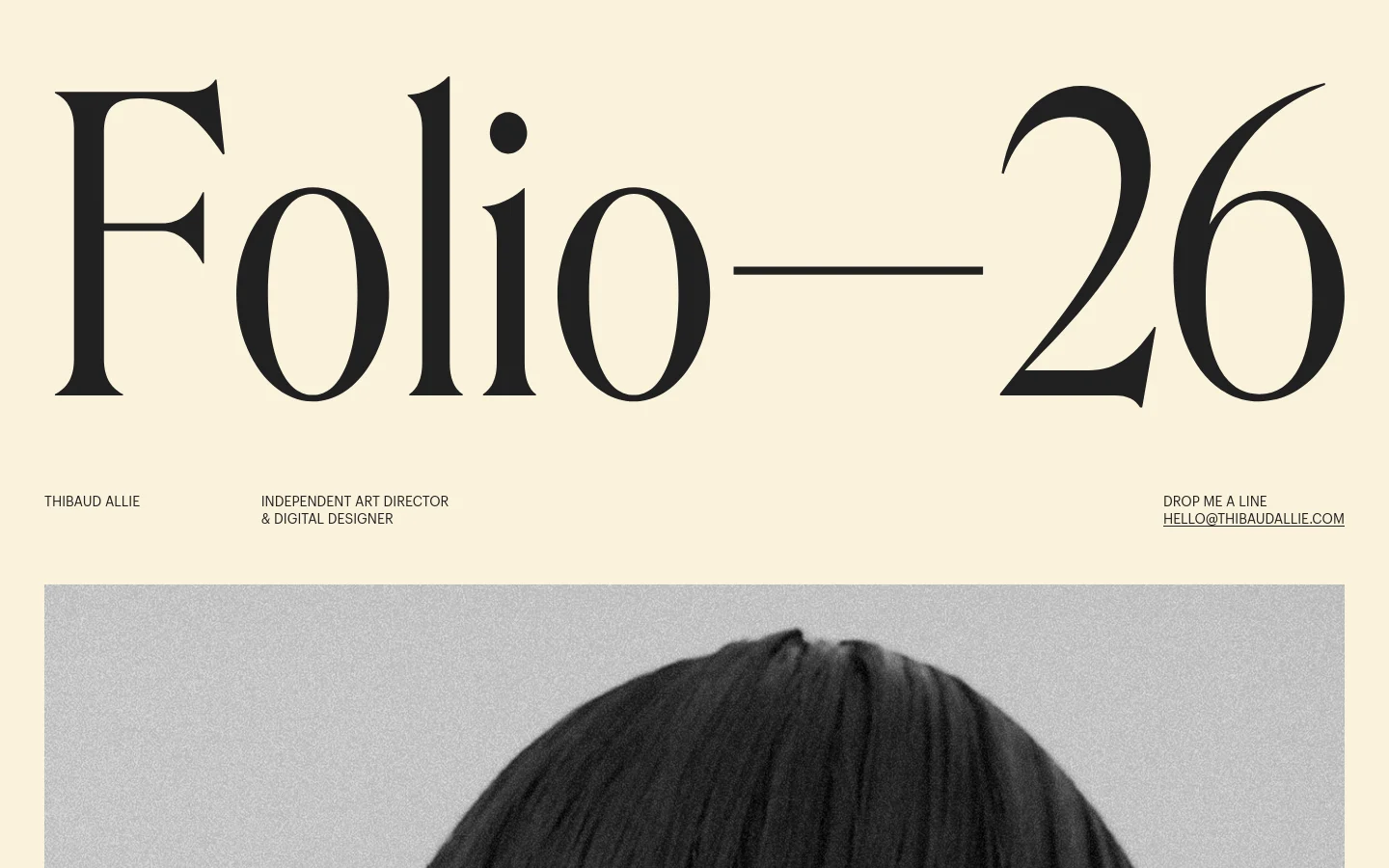 A minimalist portfolio homepage with a cream background and large, elegant serif typography. The hero section features the title 'Folio—26' in massive black text, followed by a navigation bar containing the name 'Thibaud Allie', professional title, and contact email. Below the header is a large, colorful project preview image of a person in a patterned coat against a landscape background.
