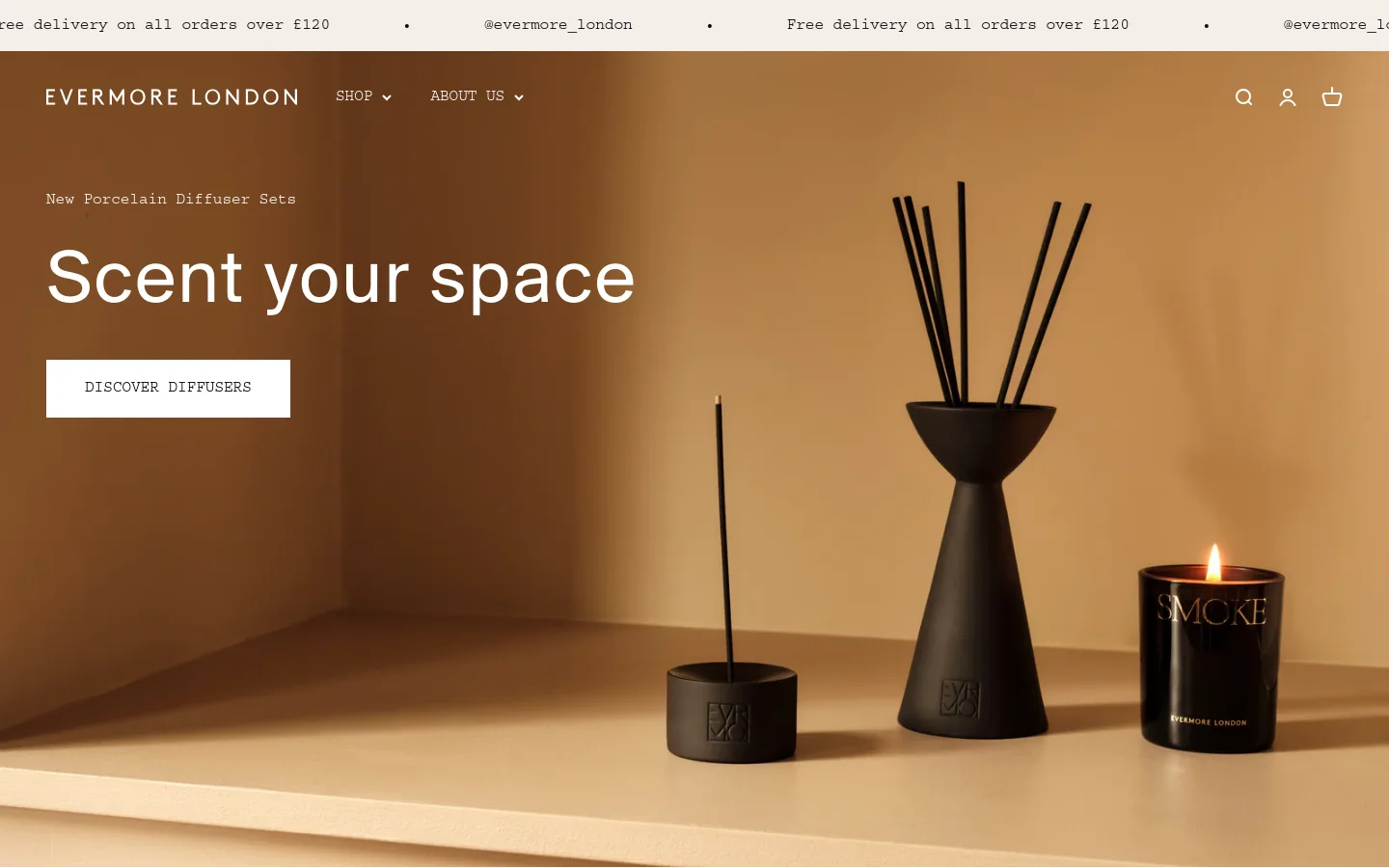 The Evermore London homepage features a warm, earth-toned hero image of black porcelain diffusers and a lit candle on a shelf. A large headline reads 'Scent your space' above a white 'DISCOVER DIFFUSERS' call-to-action button. The navigation menu at the top includes links for Shop and About Us, alongside search, account, and cart icons.