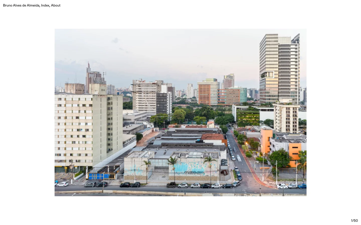 The desktop homepage features a minimalist white layout with the name 'Bruno Alves de Almeida' and navigation links 'Index' and 'About' at the top. A large, wide-format hero image displays a cityscape with various apartment buildings under a pale sky, followed by a vertical gallery of art installation photographs.