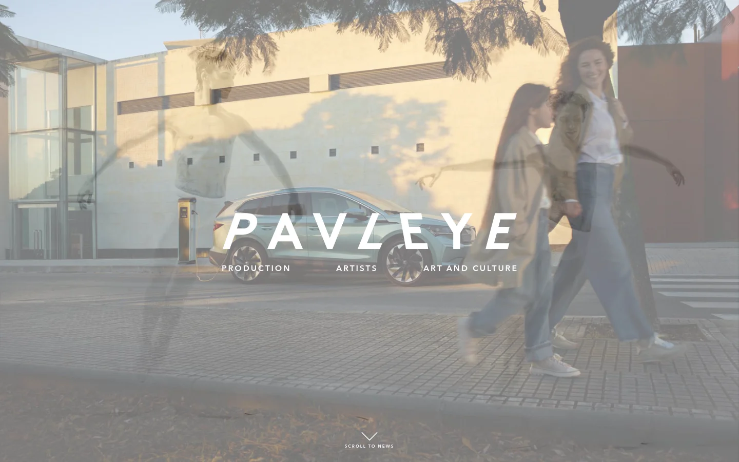 The desktop homepage features a large, cinematic hero image of a silver car parked in front of a modern building with people walking by in a motion blur. The white 'PAVLEYE' logo is centered, with the subtext 'PRODUCTION ARTISTS ART AND CULTURE' underneath, and a 'SCROLL TO NEWS' prompt at the bottom.