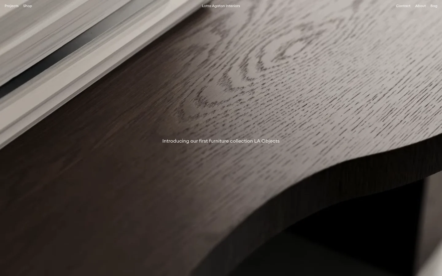 The desktop homepage features a minimalist design with a large, high-resolution hero image of dark wood grain texture. Navigation links for Projects, Shop, Contact, About, and Bag are placed at the top corners, with the brand name 'Lotta Agaton Interiors' centered. A central text overlay reads, 'Introducing our first furniture collection LA Objects.'