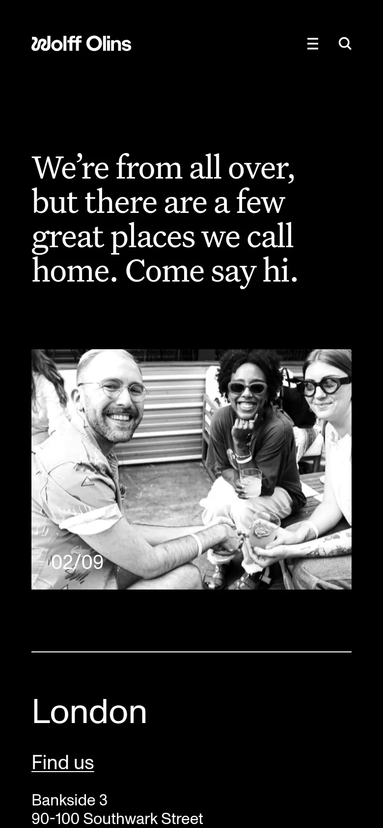 The mobile version maintains the black background and large white serif headline. The layout is vertically stacked, showing the headline followed by a single large black-and-white hero image of a group of people. The navigation is condensed into a hamburger menu and a search icon at the top.