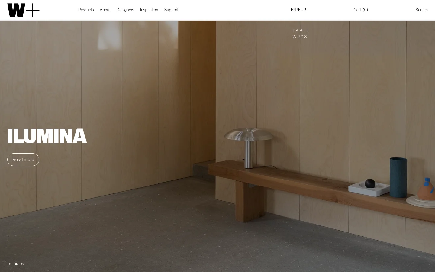 The desktop homepage features a minimalist design with a large hero image of the ILUMINA table lamp on a wooden bench against a light wood wall. A navigation bar at the top includes the W+ logo, Products, About, Newsletters, Inspiration, Support, and a shopping cart. A 'Read more' call to action button is overlaid on the hero image.