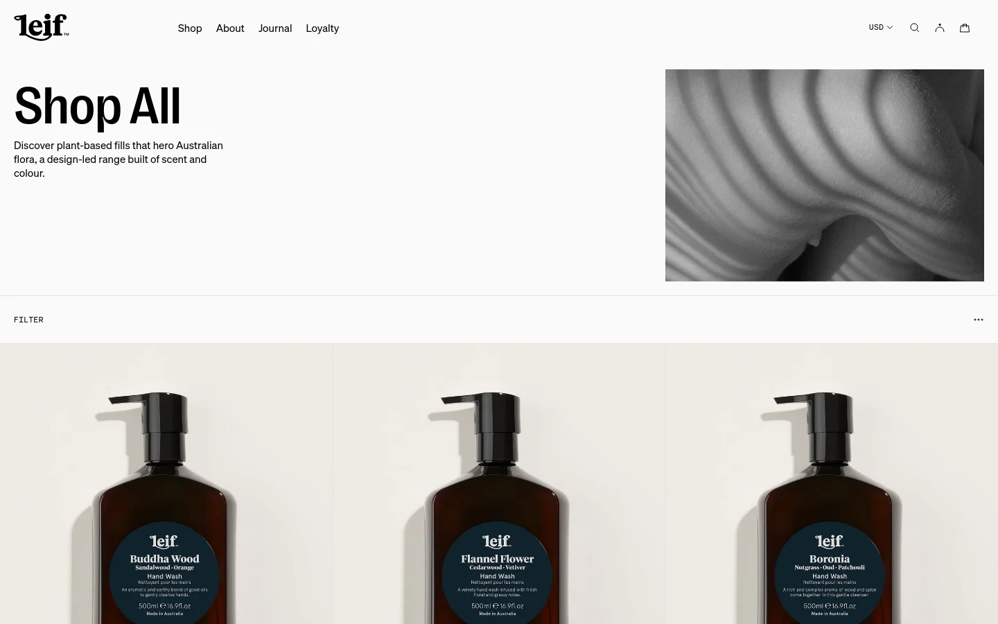 The desktop page features a large 'Shop All' headline with a descriptive subtext next to a wide, black-and-white hero image of flowing fabric. Below, a product grid displays various hand washes with high-quality product photography, prices, and descriptions on a clean white background. A filter option is available above the product listings.