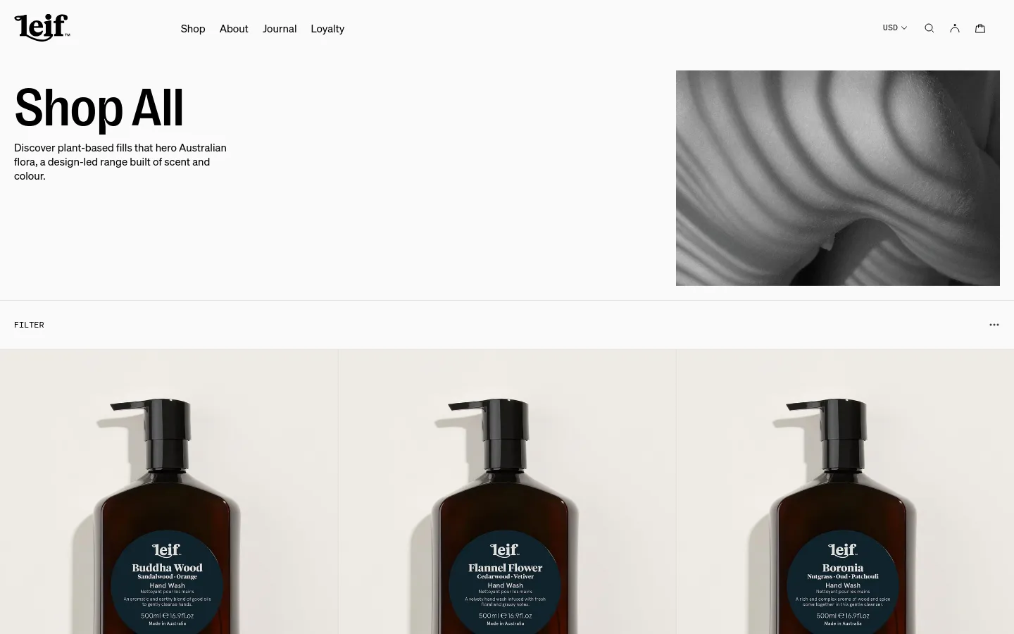 The desktop page features a large 'Shop All' headline with a descriptive subtext next to a wide, black-and-white hero image of flowing fabric. Below, a product grid displays various hand washes with high-quality product photography, prices, and descriptions on a clean white background. A filter option is available above the product listings.