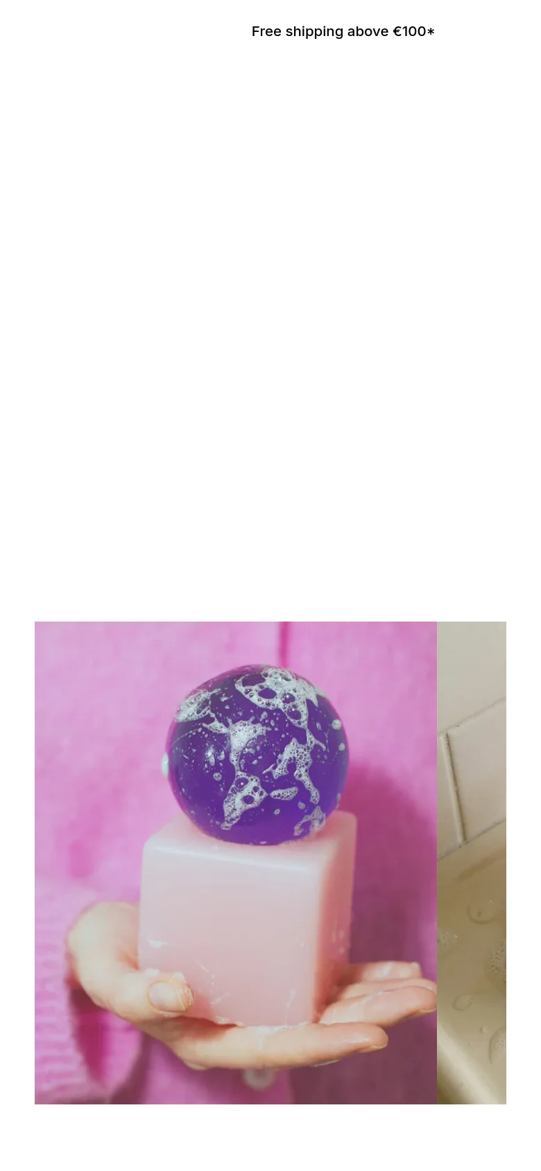 The mobile version presents a vertically stacked layout with the announcement bar at the top. The hero text and 'VIEW COLLECTION' link are centered above a large, close-up image of a purple spherical soap resting on a pink cube, emphasizing the product's texture and sculptural form.