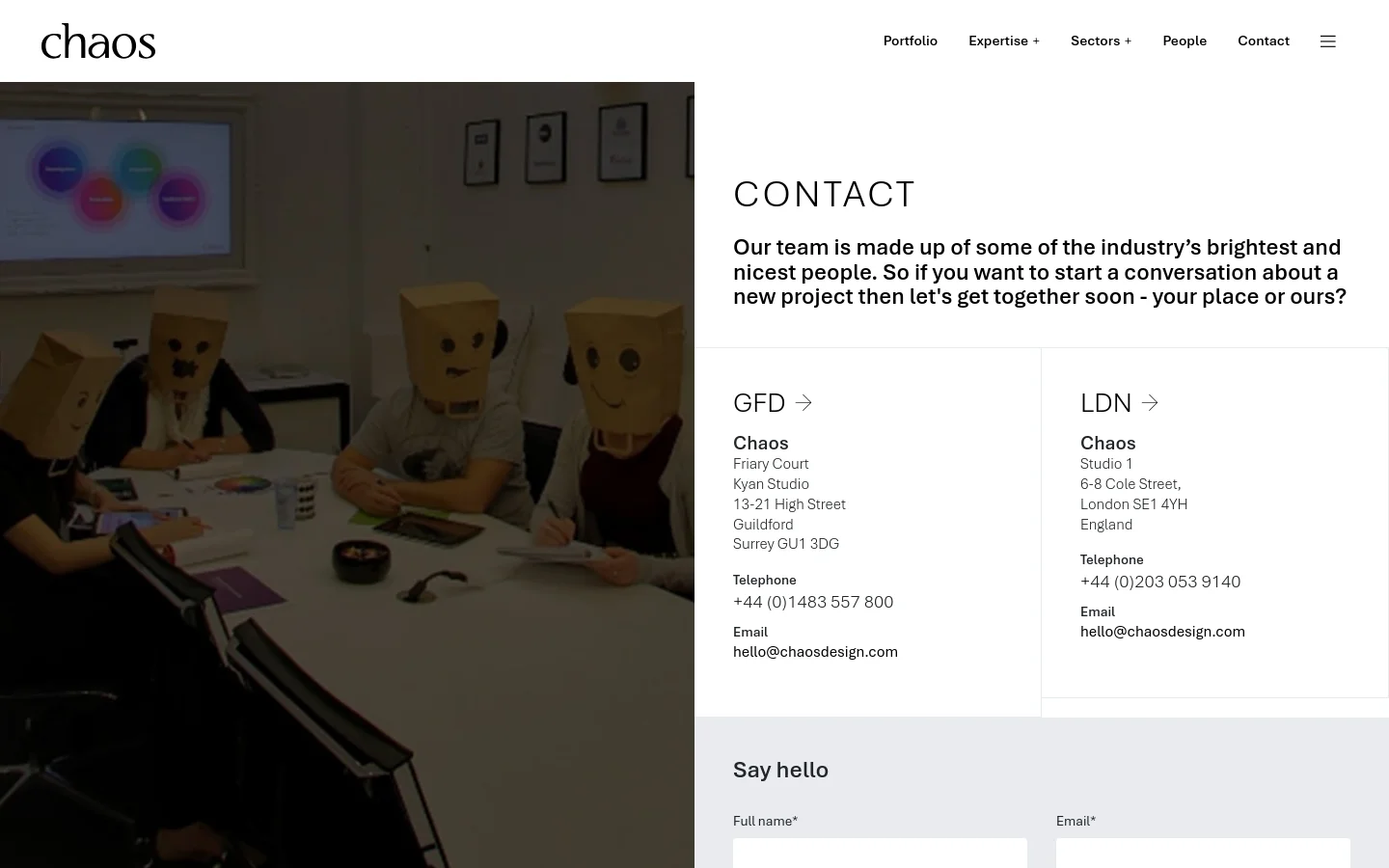 The desktop page features a split layout with a large hero image on the left showing people in a meeting wearing paper bags over their heads. On the right, a white section contains the headline 'CONTACT', an introductory paragraph, and two side-by-side contact cards for the Guildford (GFD) and London (LDN) offices. The navigation menu is at the top right against a white background.