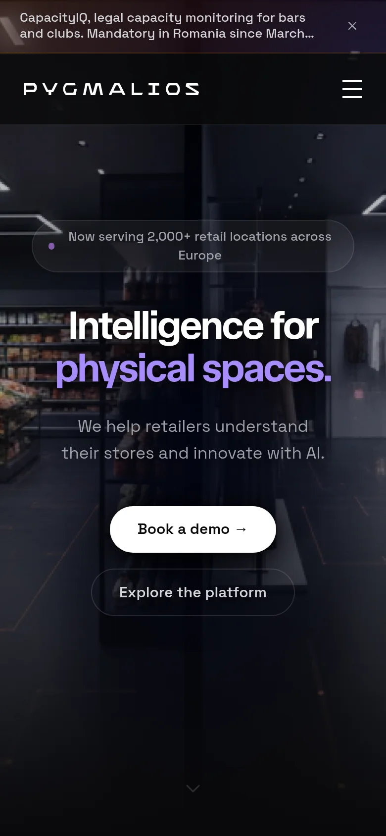 The mobile version uses a simplified layout with a hamburger menu icon in the top right and the Pygmalios logo on the left. The hero section remains centered, featuring the main headline and two large, stacked buttons for 'Book a demo' and 'Explore the platform' over a darkened retail store background.