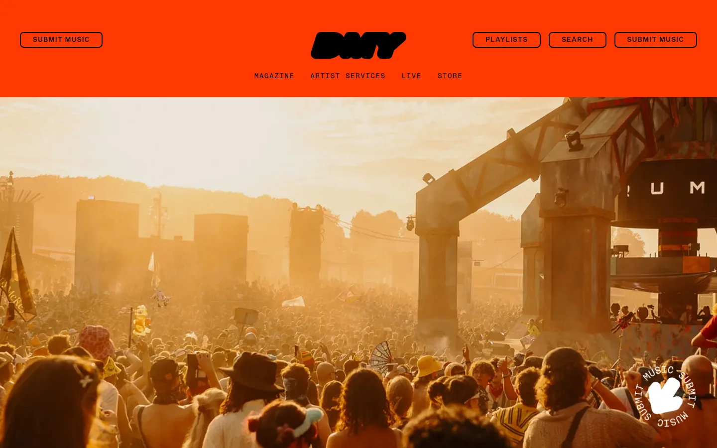 The DMY homepage features a bright orange header with a black logo and navigation links for Magazine, Artist Services, Live, and Store. A large hero image shows a crowded music festival at sunset with large industrial stage structures. Below the hero, a content slider displays music-related articles with large images and headlines.