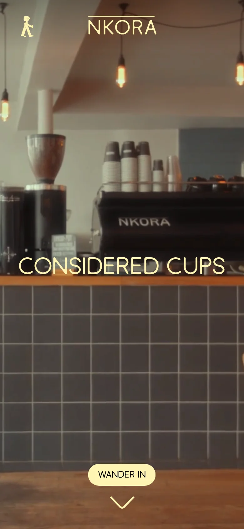 The mobile version uses a vertical layout with a close-up hero image of a coffee shop interior, showing an espresso machine and hanging lights. The 'CONSIDERED CUPS' headline and 'WANDER IN' button are centered, and the navigation is condensed into a simplified header with a person icon and the NKORA logo.