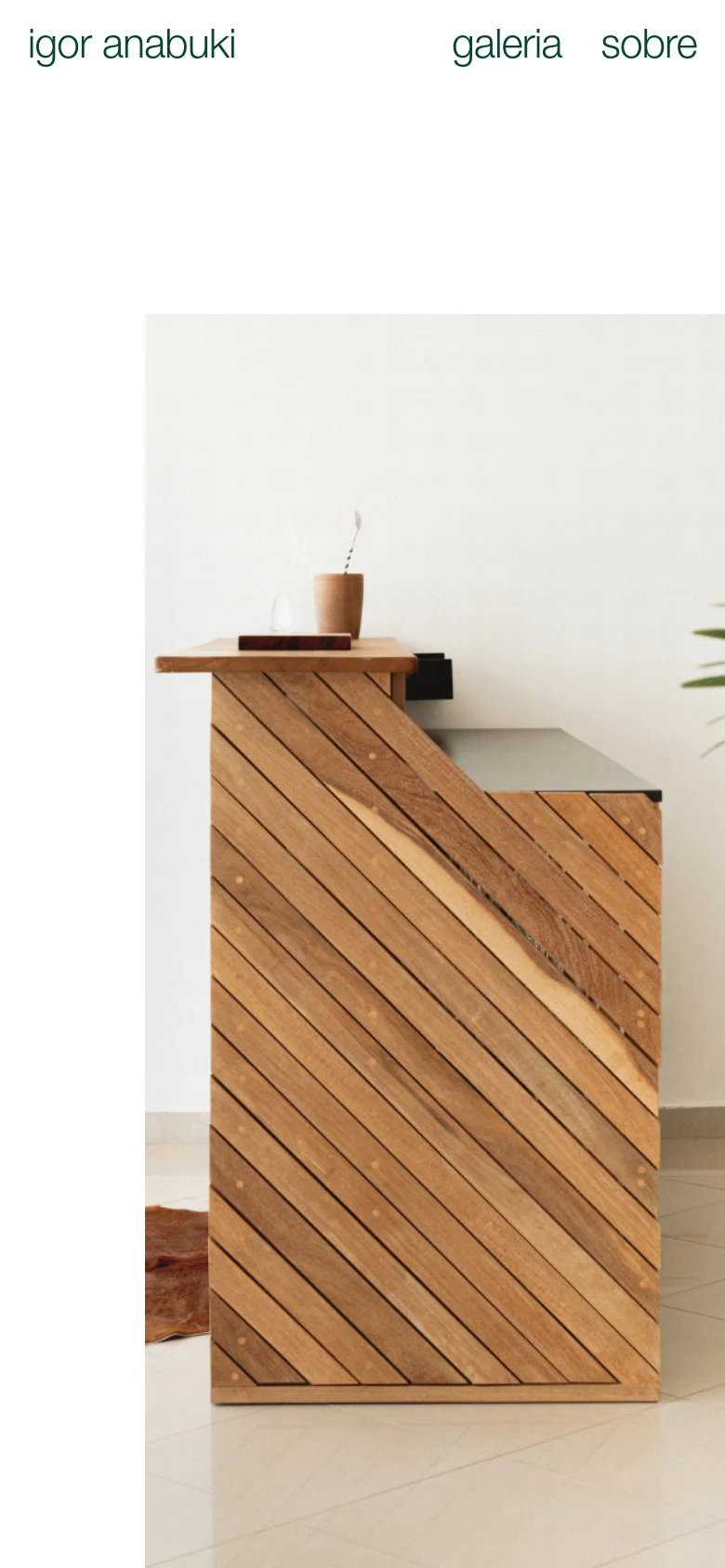 The mobile version maintains the minimalist aesthetic with a white background and black text. The navigation links 'galeria' and 'sobre' are positioned at the top right, while the brand name 'igor anabuki' is at the top left. The large hero image of the wooden furniture is scaled to fit the vertical screen, occupying most of the viewport.