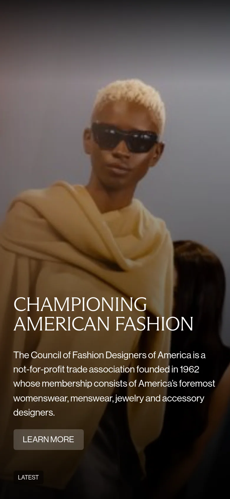 The mobile version presents a vertically oriented view of the hero section, with the headline 'CHAMPIONING AMERICAN FASHION' and descriptive text centered over a close-up of a model wearing sunglasses and a yellow wrap. The 'LEARN MORE' button is prominently placed below the text, and the 'LATEST' label is located at the bottom left.
