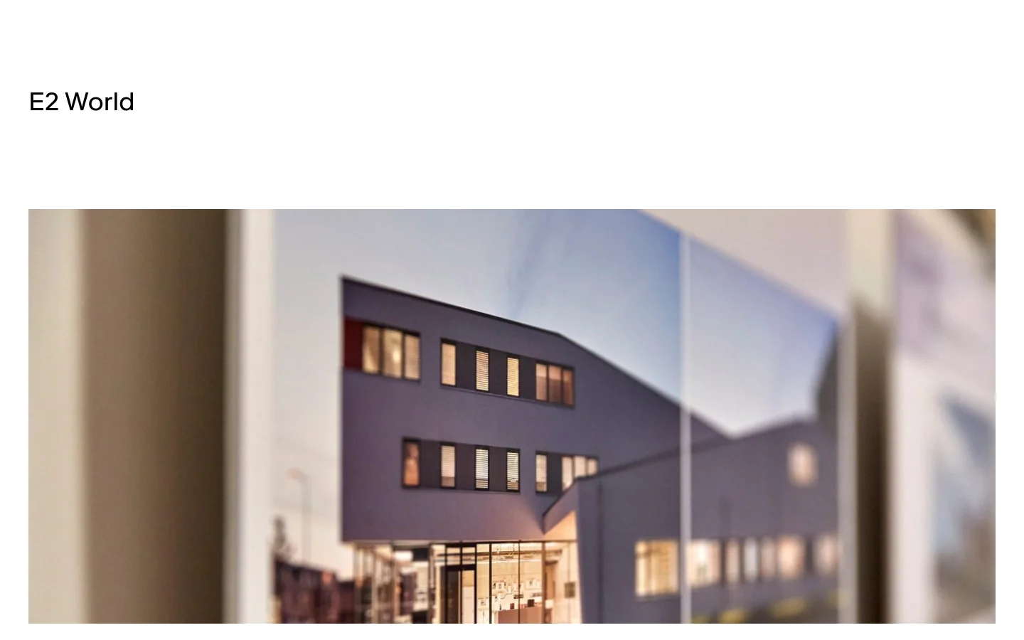 The desktop page for E2 World features a clean, minimalist layout with a large hero image of a modern architectural building. Below the hero, content is organized into vertical sections, each containing a wide rectangular image, a bold headline, and a text link. The color palette is neutral, focusing on high-quality photography of design and architecture.