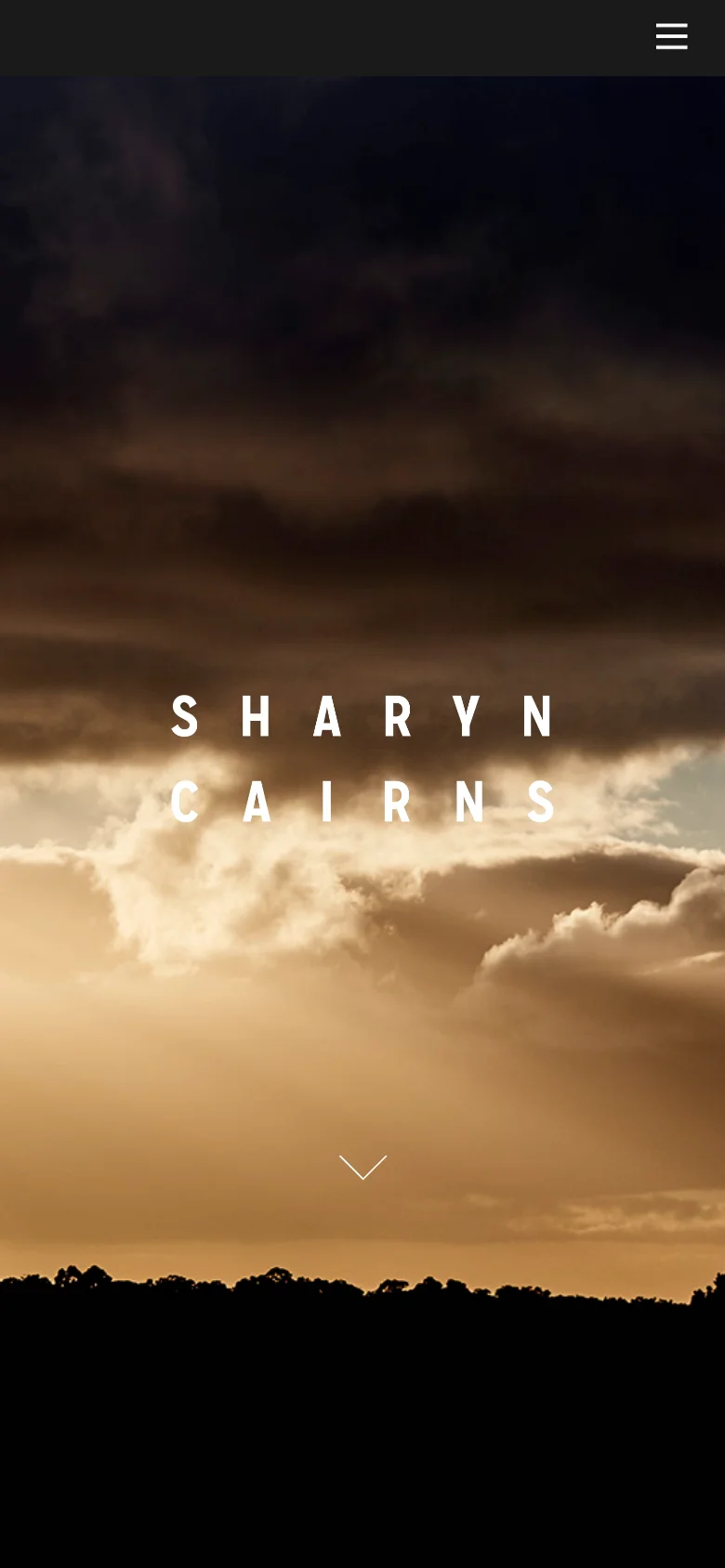 The mobile version displays the same dramatic sunset hero image with centered white text reading 'SHARYN CAIRNS'. The layout is vertically oriented, featuring a simplified dark header with a hamburger menu icon and a prominent white down-arrow icon centered near the bottom to encourage scrolling.