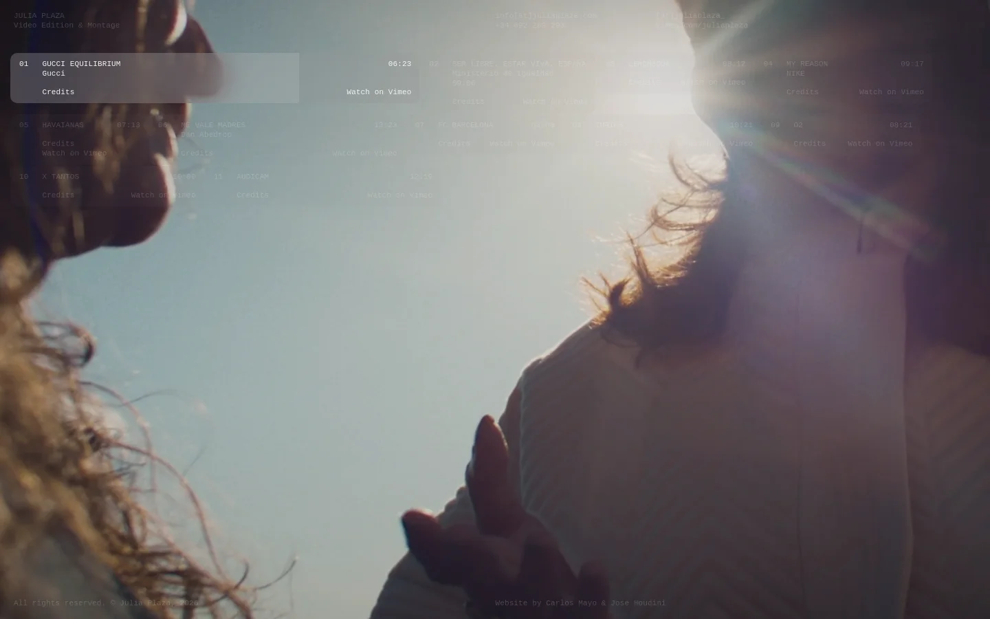 A minimalist portfolio website for Julia Plaza, featuring a large, cinematic background image of a person in soft sunlight. The layout consists of a header with the name and contact details, followed by a grid of video projects listed by number, title, client, and duration. Each project includes a 'Credits' link and a 'Watch on Vimeo' call to action against a muted, professional aesthetic.