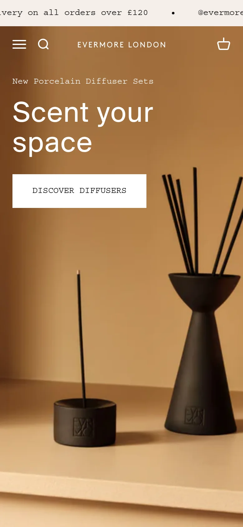 The mobile version presents a vertically stacked layout with a condensed header containing a hamburger menu, search icon, and shopping bag. The hero section features the same 'Scent your space' headline and 'DISCOVER DIFFUSERS' button against a warm, minimalist background of black fragrance products.