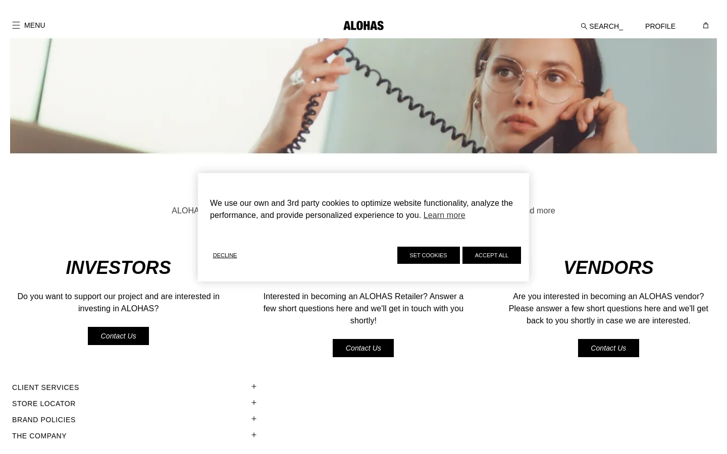 The desktop page features a wide hero banner showing a woman with glasses using a telephone, set against a neutral background. Below the banner, the headline 'INQUIRIES' is followed by three distinct sections for Investors, Wholesale, and Vendors, each with a brief description and a black 'Contact Us' button. The layout is clean with ample white space and a minimalist navigation bar at the top.