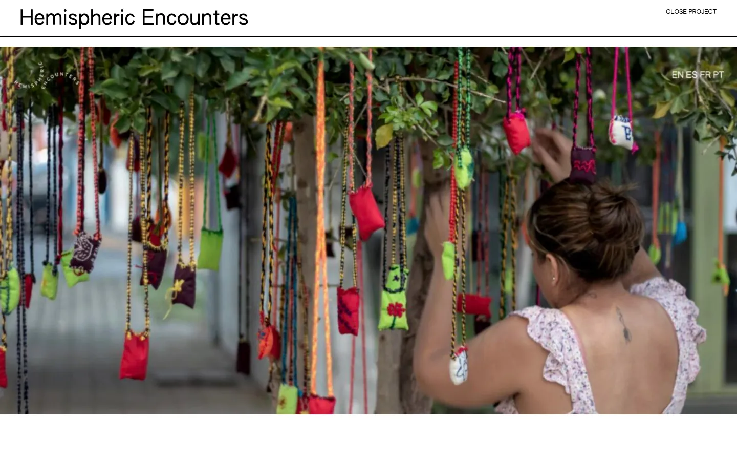 The desktop page features the headline 'Hemispheric Encounters' with a 'CLOSE PROJECT' link in the top right. Below the header is a large hero image of a person arranging colorful, hanging fabric pouches on a tree, with language options (EN, ES, FR, PT) overlaid in the top right corner.