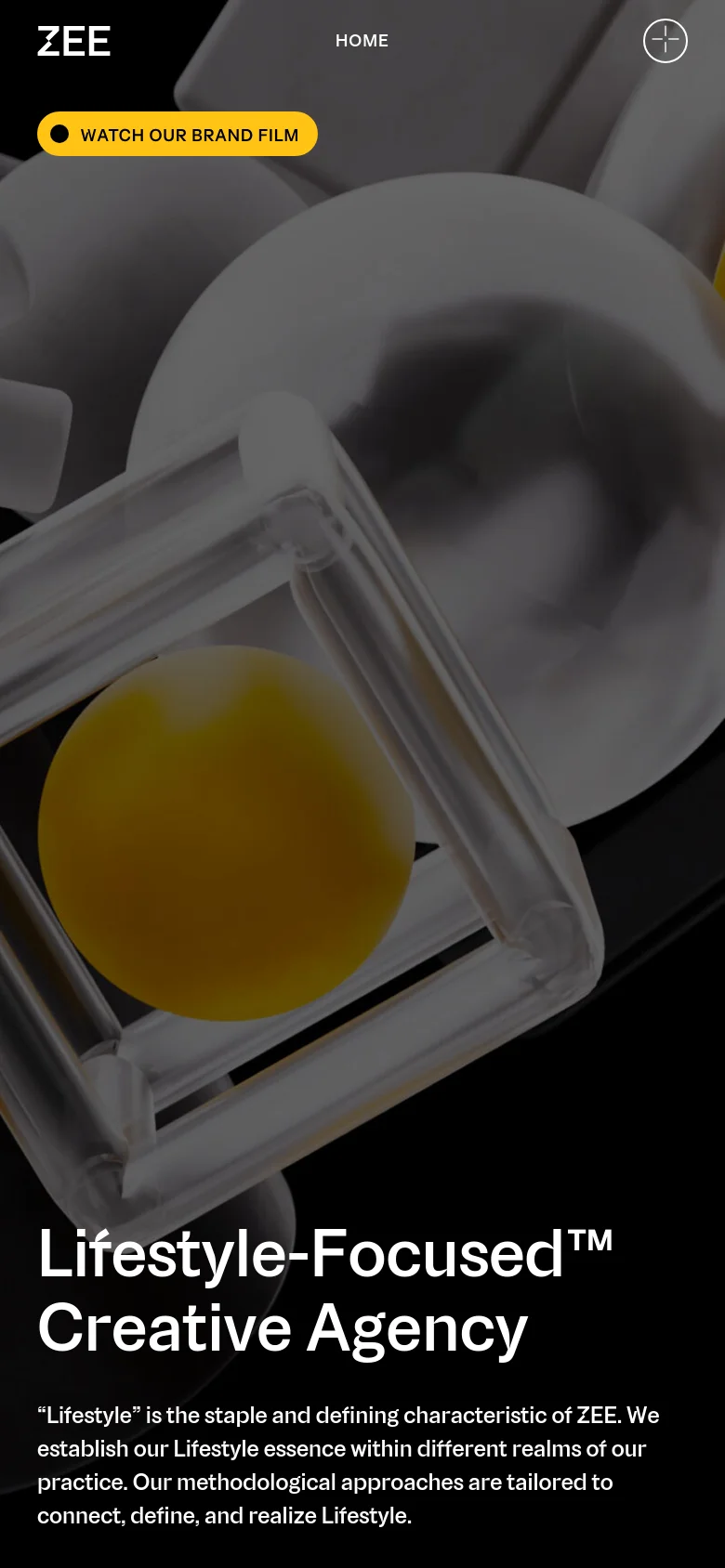 The mobile version displays a close-up, abstract shot of metallic and yellow spherical objects under a dark overlay. The headline 'Lifestyle-Focused™ Creative Agency' is prominently displayed in white, followed by a brief introductory paragraph about the agency's essence.