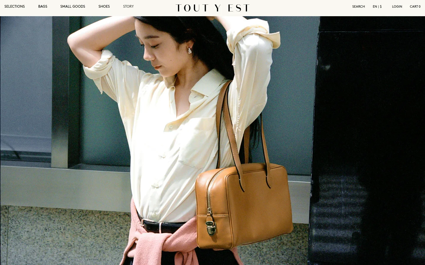 The desktop homepage features a minimalist design with a large hero image of a woman wearing a cream shirt and carrying a tan leather bag. A navigation bar at the top includes links for Selections, Bags, Small Goods, Shoes, and Story, alongside search and login options. Below the hero image, a 'New Arrivals' section displays product grid items with titles, colors, and prices.