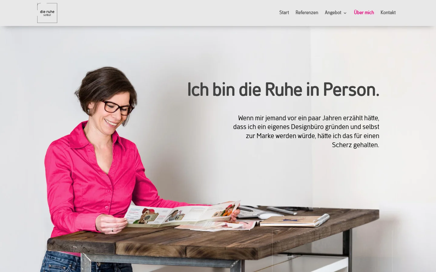 Desktop view of the 'Über Mich' page featuring a clean, minimalist layout with a light gray background. A large hero image shows a smiling woman in a bright pink shirt looking at a magazine at a wooden desk, accompanied by the headline 'Ich bin die Ruhe in Person.' A white navigation bar at the top contains the logo on the left and links for Start, Referenzen, Angebot, Über mich, and Kontakt on the right.