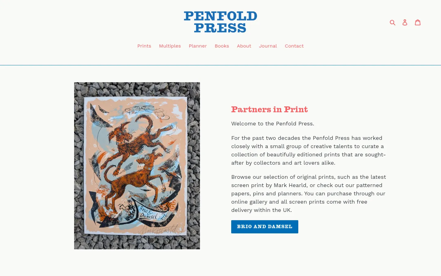 The Penfold Press homepage features a clean white background with a large hero image on the left showing a colorful print of two dogs on a pebbled surface. To the right, the headline 'Partners in Print' is followed by introductory text and a blue call-to-action button labeled 'BRIO AND DAMSEL'. The top navigation includes the brand logo in blue and links for Prints, Multiples, Planner, Books, About, Journal, and Contact.