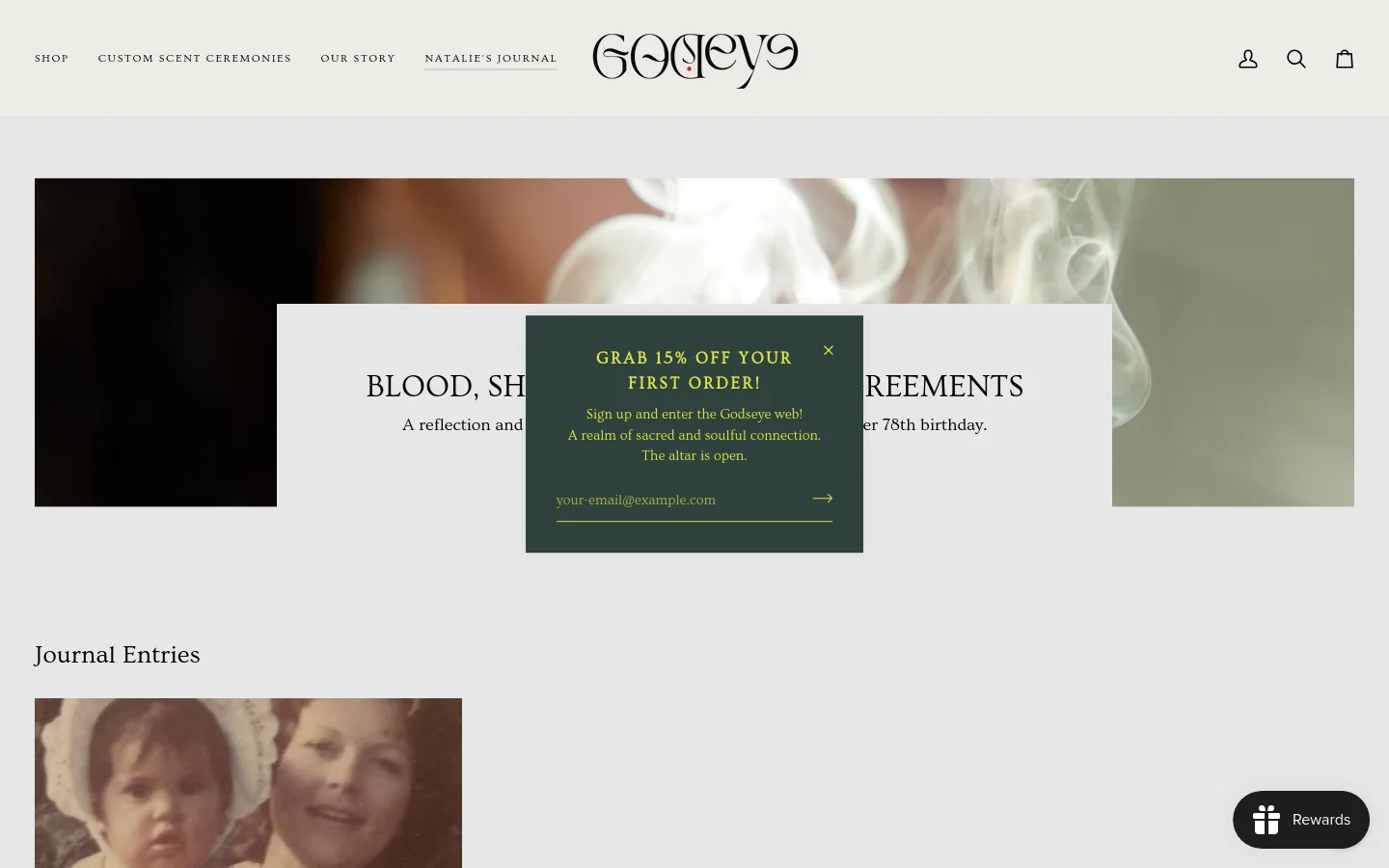 The desktop view of Natalie's Journal features a minimalist design with a large hero image of ethereal white smoke against a dark background. A centered white overlay contains the article title 'BLOOD, SHEDDING, & SACRED AGREEMENTS' and a brief description, partially obscured by a dark green promotional pop-up offering 15% off. Below, the 'Journal Entries' section begins with a vintage-style photograph of a child and an adult.