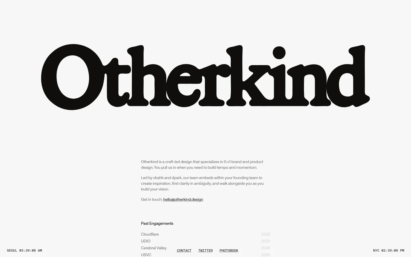 The desktop homepage features a minimalist design with a large, bold black 'Otherkind' logo centered at the top against a light gray background. Below the logo, text describes the design studio's mission, followed by a 'Past Engagements' list with company names and years aligned to the sides. Navigation links like 'CONTACT' and 'TWITTER' are positioned at the bottom, flanking a timestamp.