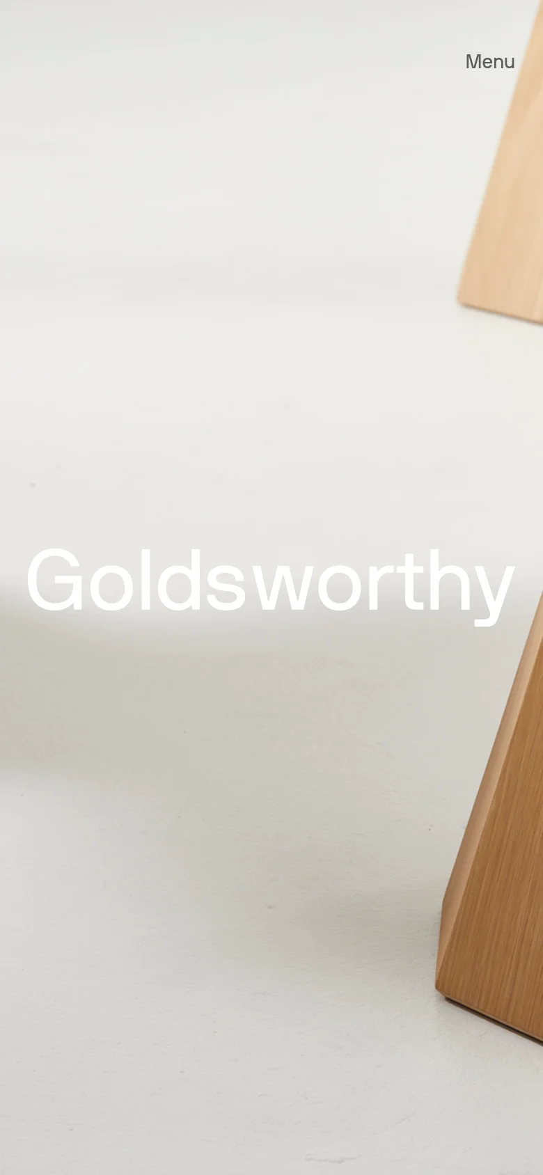 The mobile version maintains the minimalist aesthetic, showing a close-up, vertically oriented view of the wooden furniture. The 'Goldsworthy' headline is prominently centered, and the navigation is condensed into a simple 'Menu' link at the top right.