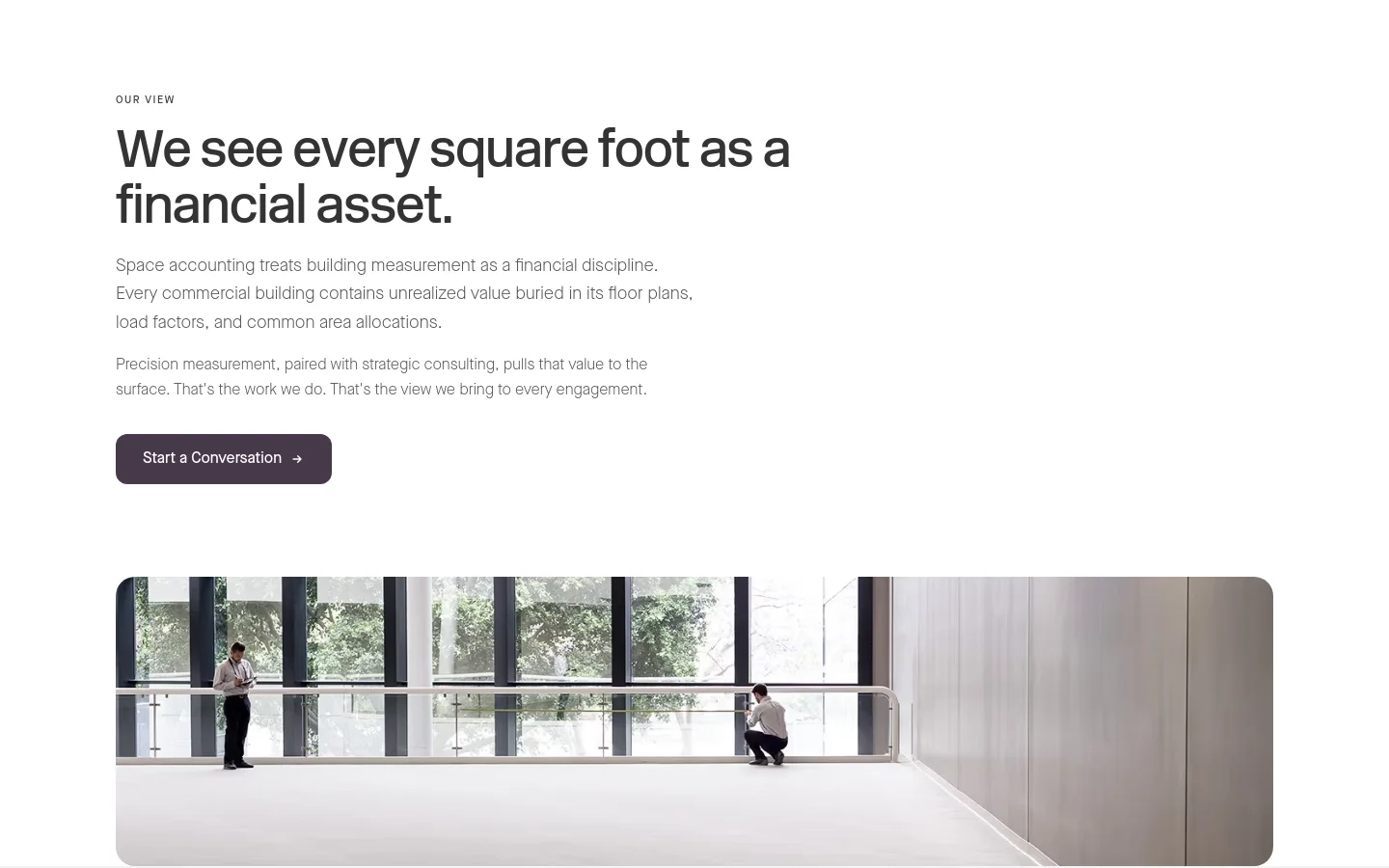 The desktop page features a minimalist white layout with the headline 'We see every square foot as a financial asset' in large, dark grey sans-serif font. Below the text is a dark purple 'Start a Conversation' button, followed by a wide, cinematic photograph of a modern, bright office interior with large windows and two people.