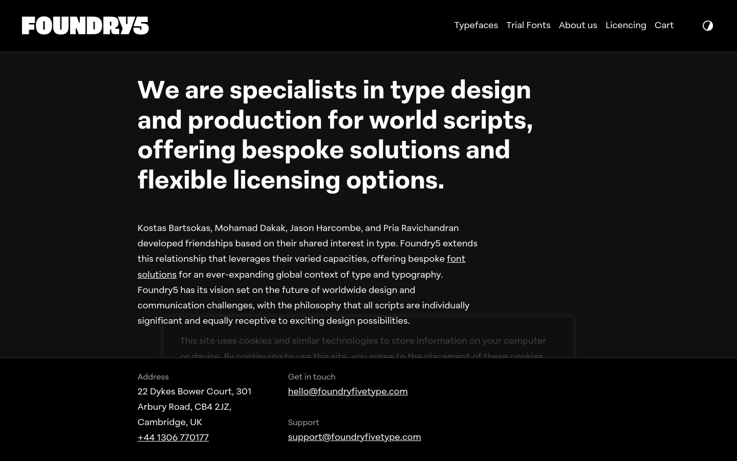The About Us page features a minimalist dark theme with white text. A large, bold headline introduces the studio's specialty in world scripts, followed by several paragraphs of text and contact information in the footer. The layout is spacious with a clean navigation bar at the top containing links for Typefaces, Trial Fonts, About us, Licensing, and Cart.