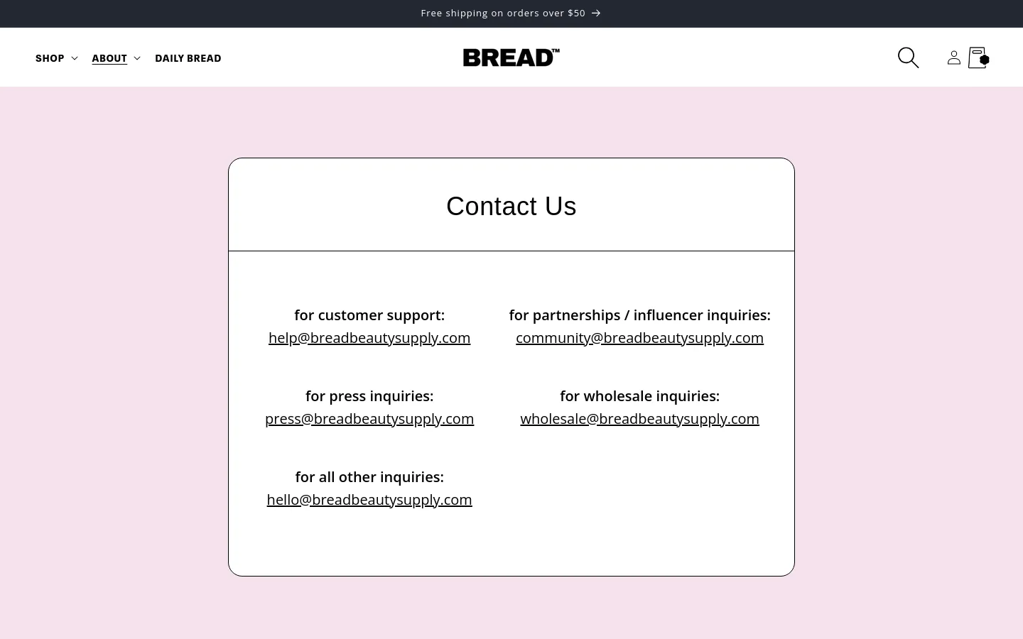 The desktop Contact Us page features a minimalist design with a light pink background and a large white central container. Inside the container, various contact email addresses are organized into two columns under bold headings for customer support, partnerships, press, wholesale, and general inquiries. The top navigation bar is white and includes the BREAD logo, shop and about dropdowns, a search icon, and a user account icon.