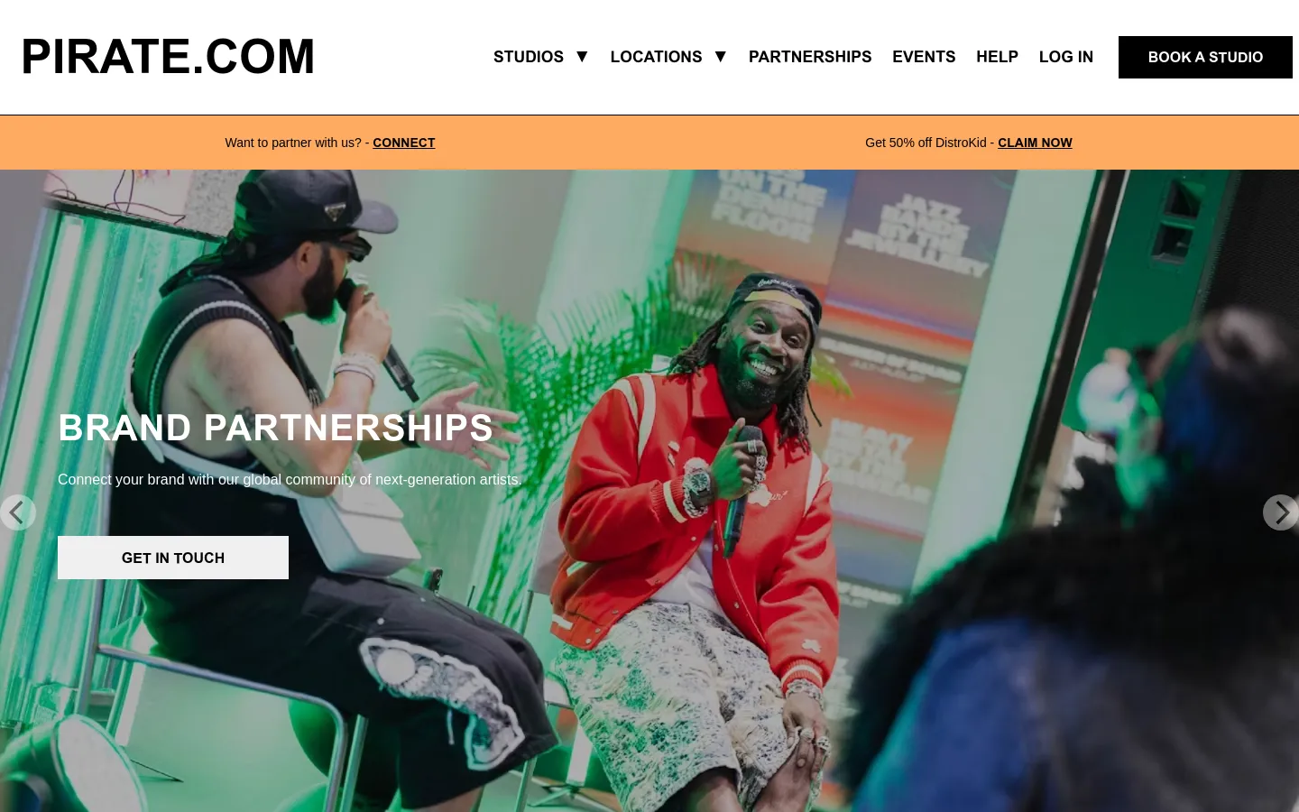 The Brand Partnerships page features a large hero image of artists in a vibrant, green-lit studio setting with the headline 'BRAND PARTNERSHIPS' and a 'GET IN TOUCH' button. Below, the layout includes sections for artist community outreach and case studies like Selfridges and Relentless, interspersed with high-quality photography of musicians and DJs. The design uses a dark theme with bold white typography and orange announcement banners at the top.