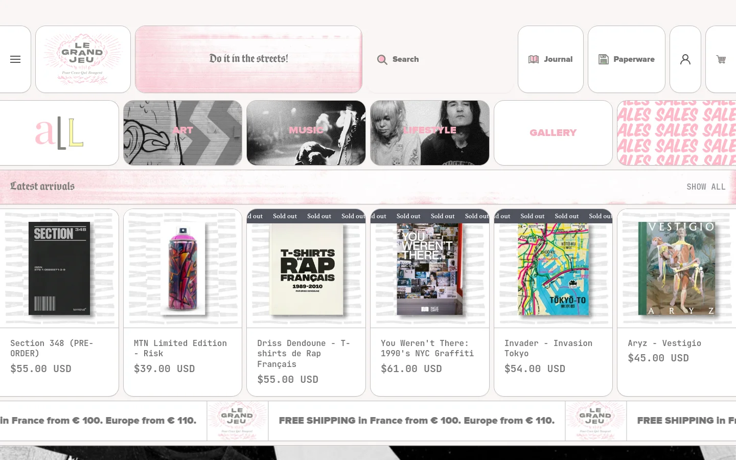 The desktop homepage for Le Grand Jeu bookstore features a light pink textured header with the slogan 'Do it in the streets!' and a navigation menu including Journal and Paperware. Below the header, a grid of large category tiles for Art, Music, Lifestyle, and Gallery is displayed, followed by a 'Latest arrivals' section showing a horizontal row of product cards with images, titles, and prices.