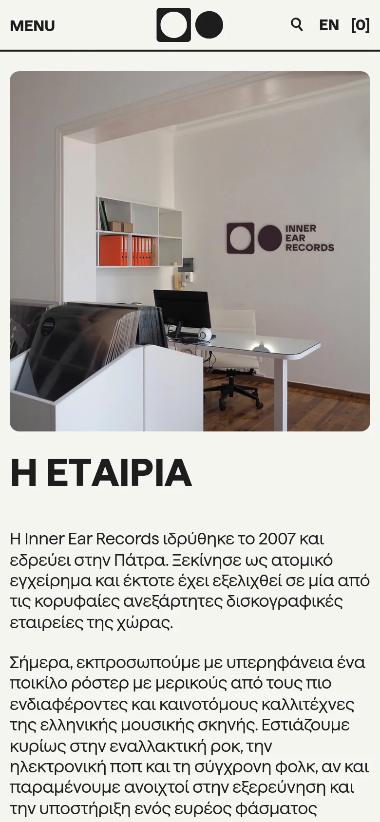 The mobile version uses a vertical stack layout with a simplified header containing a 'MENU' button and the company logo. The hero image of the office is displayed full-width at the top, followed by the 'H ΕΤΑΙΡΙΑ' headline and the descriptive text below it in a single column.