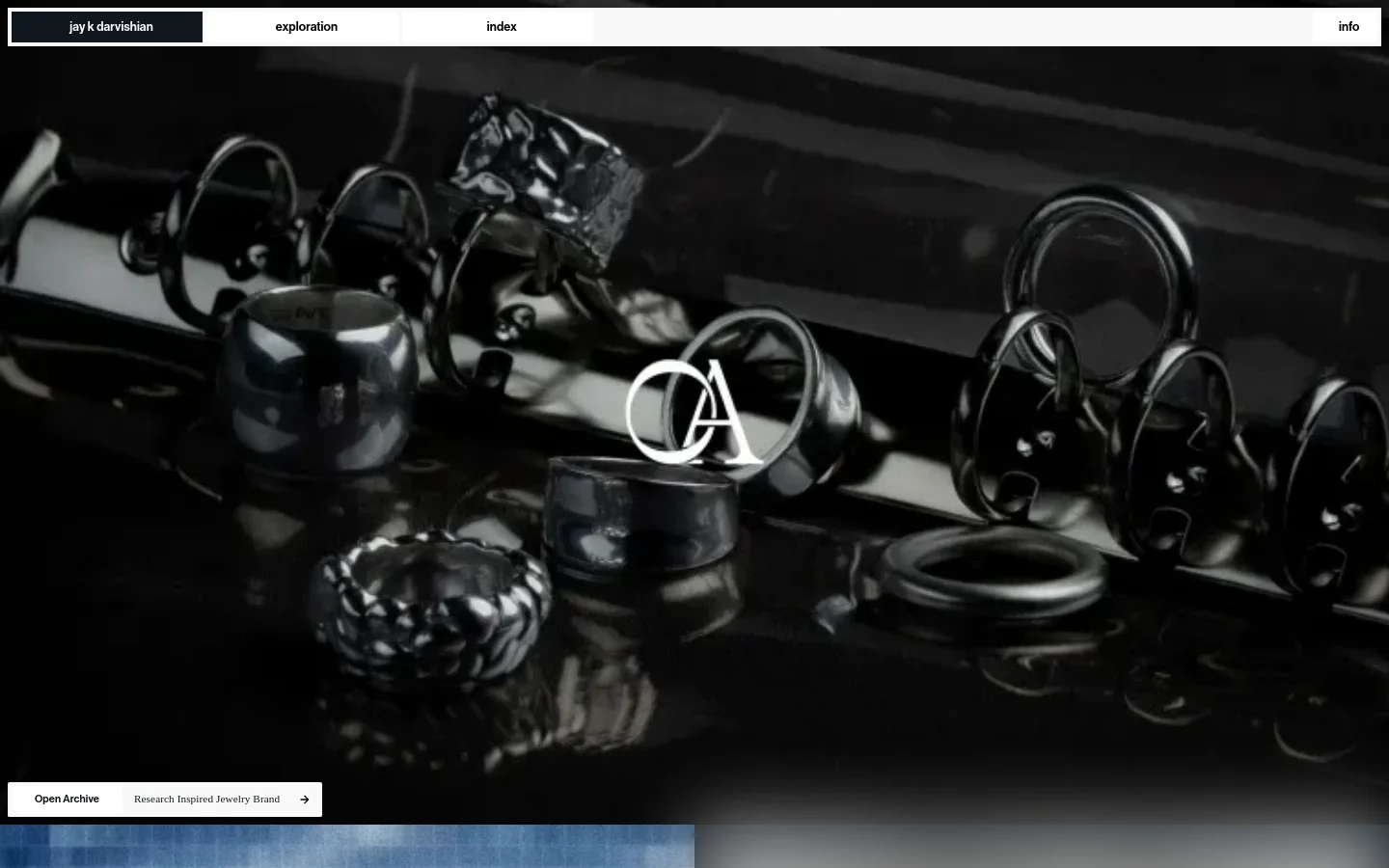A minimalist portfolio website with a dark theme and a top navigation bar containing links for jay k darvishian, exploration, index, and info. The hero section features a large, high-contrast close-up image of silver rings on a reflective black surface with the white initials 'OA' overlaid, accompanied by a call to action for 'Open Archive: Research Inspired Jewelry Brand'.