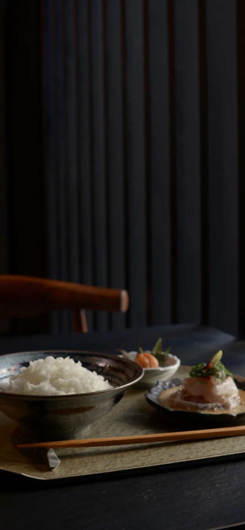 The mobile version presents a vertically oriented view of the hero image, focusing on the close-up of the sea bream dish and rice bowl. The headline and text are centered, and the navigation elements are condensed to fit the narrow screen, maintaining the dark, sophisticated color palette.