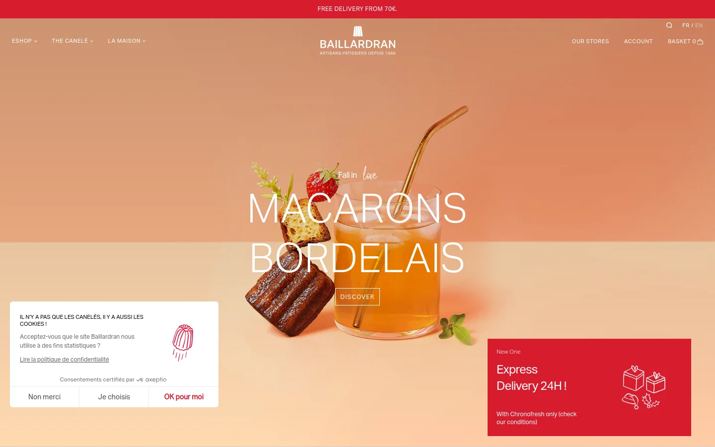 The desktop homepage features a warm, peach and cream color palette with a large hero image of Macarons Bordelais in a glass. A navigation bar at the top includes links for Shop, The Canelé, La Maison, Our Stores, Account, and Basket. A prominent 'Discover' call to action button sits over the hero image, and a cookie consent banner appears in the bottom left corner.