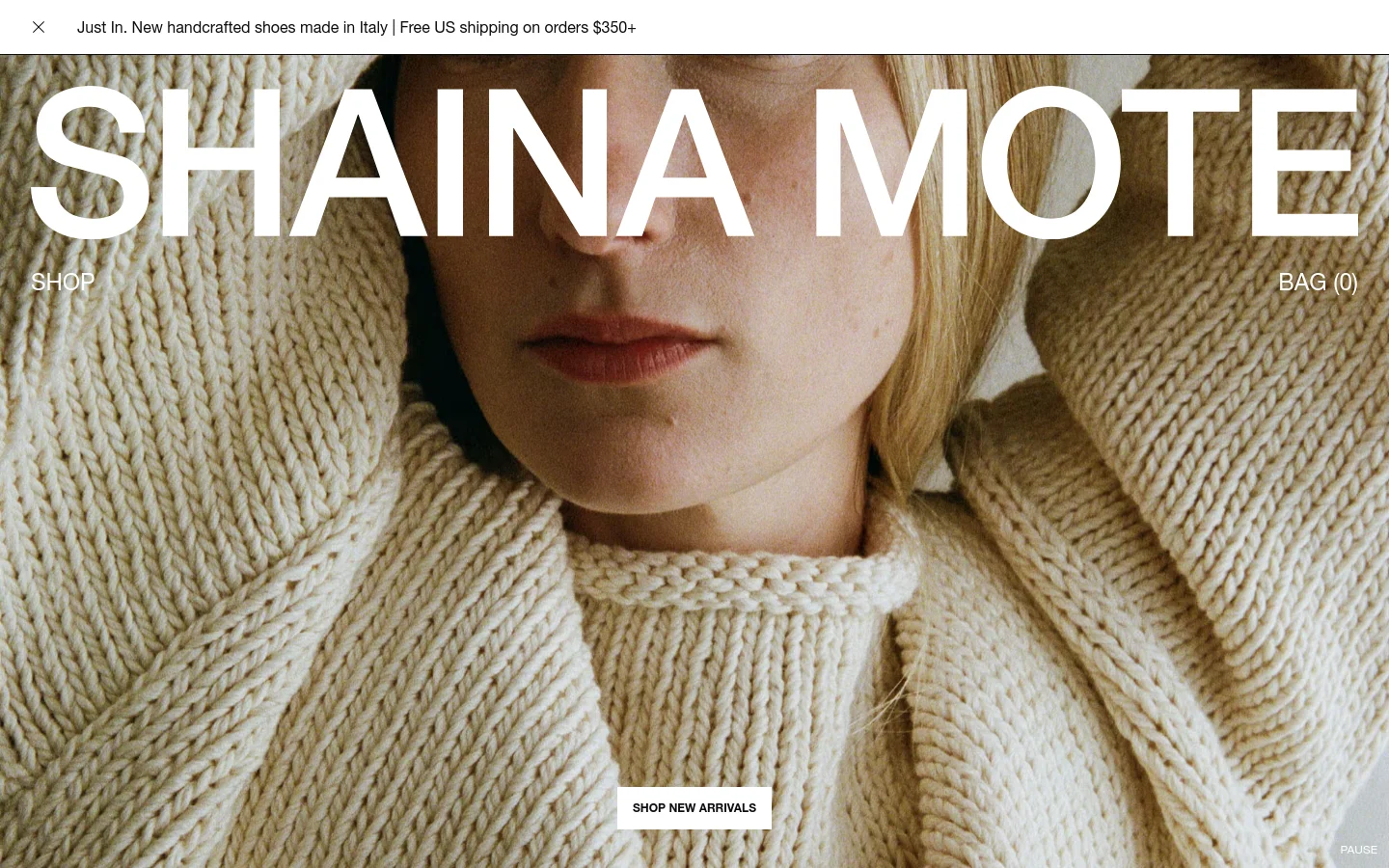 The desktop homepage features a large hero image of a person wearing a cream-colored knit sweater, with the brand name 'SHAINA MOTE' in large white capital letters overlaid. A thin announcement bar at the top mentions handcrafted shoes, and navigation links for 'SHOP' and 'BAG (0)' are positioned on either side of the center. A 'SHOP NEW ARRIVALS' call to action button is centered at the bottom of the hero section.