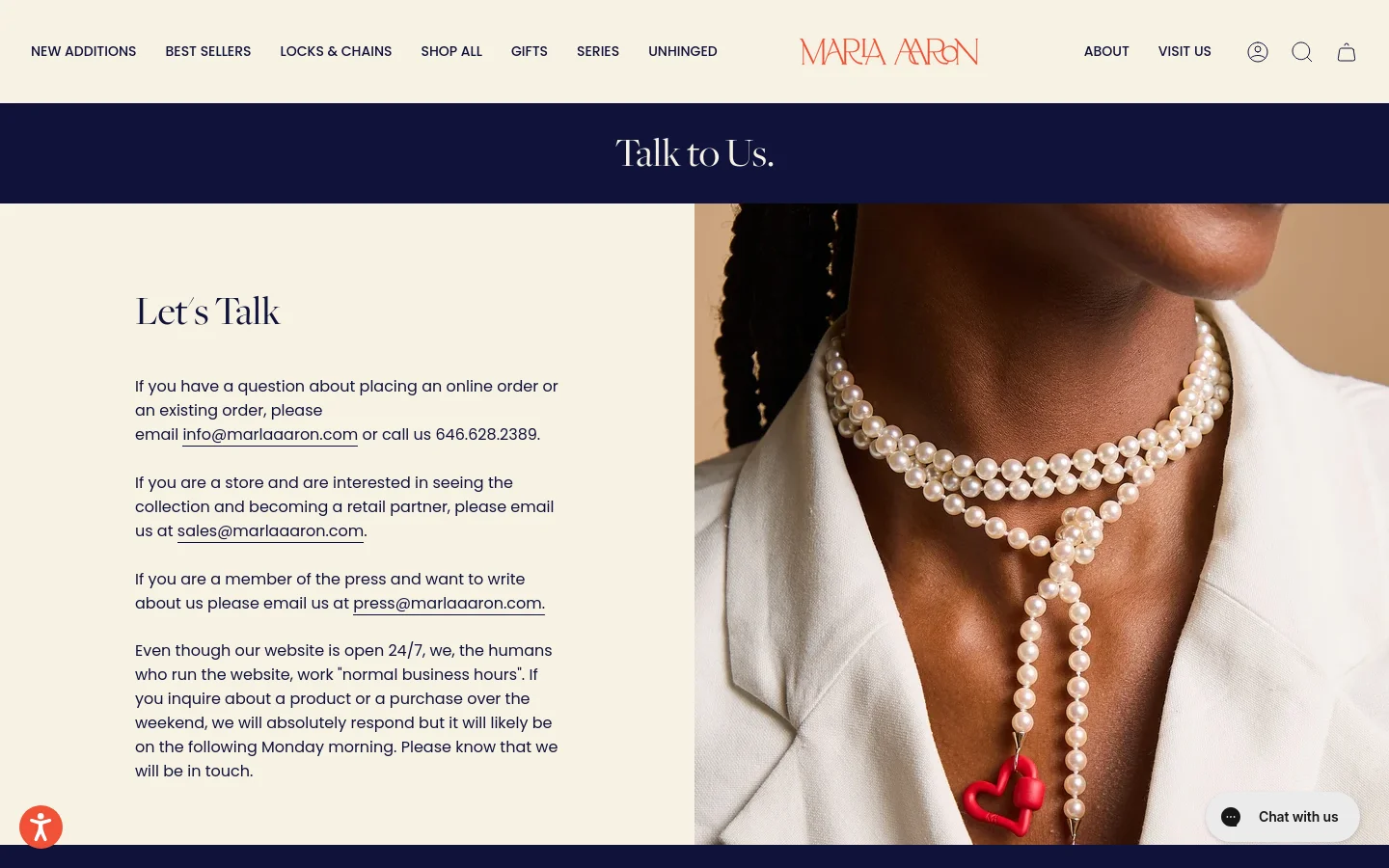 The desktop page features a minimalist design with a cream background and navy blue header containing the title 'Talk to Us.' A large hero image on the right shows a person wearing layered pearl necklaces with colorful heart charms, while the left side contains contact information and email links under the heading 'Let's Talk.'
