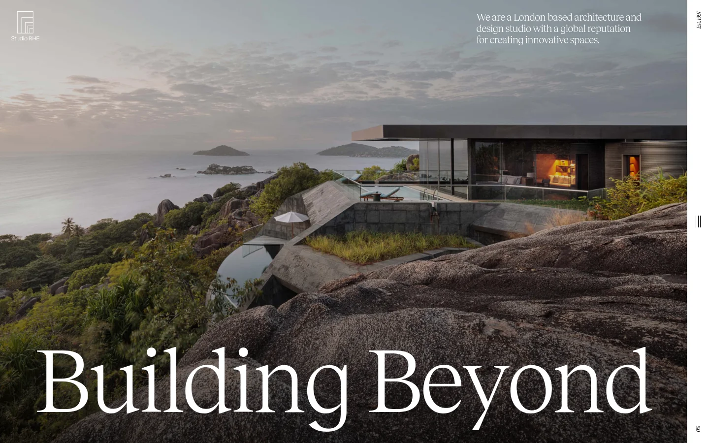 The desktop homepage features a full-width cinematic hero image of a modern luxury residence built into a rocky coastline overlooking the ocean at dusk. Large serif typography reads 'Building Beyond' in the foreground, with a brief mission statement in the top right and the Studio RHE logo in the top left.