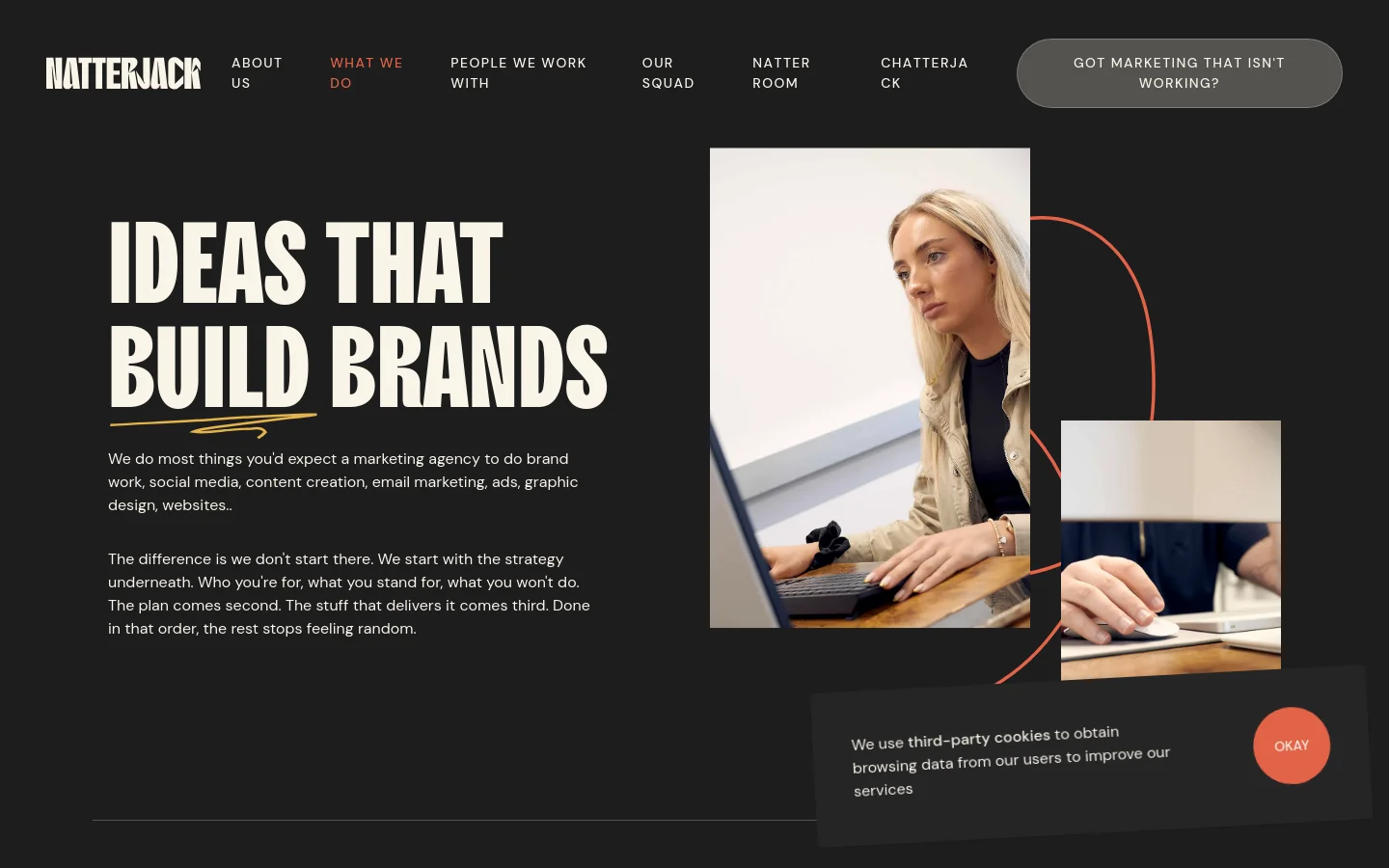 Desktop view of the 'What We Do' page featuring a dark background with bold white typography reading 'IDEAS THAT BUILD BRANDS'. To the right, a collage of two photos shows a woman working on a laptop and a close-up of hands on a desk, connected by a thin orange line. The navigation menu is at the top, and a cookie consent banner appears in the bottom right corner.