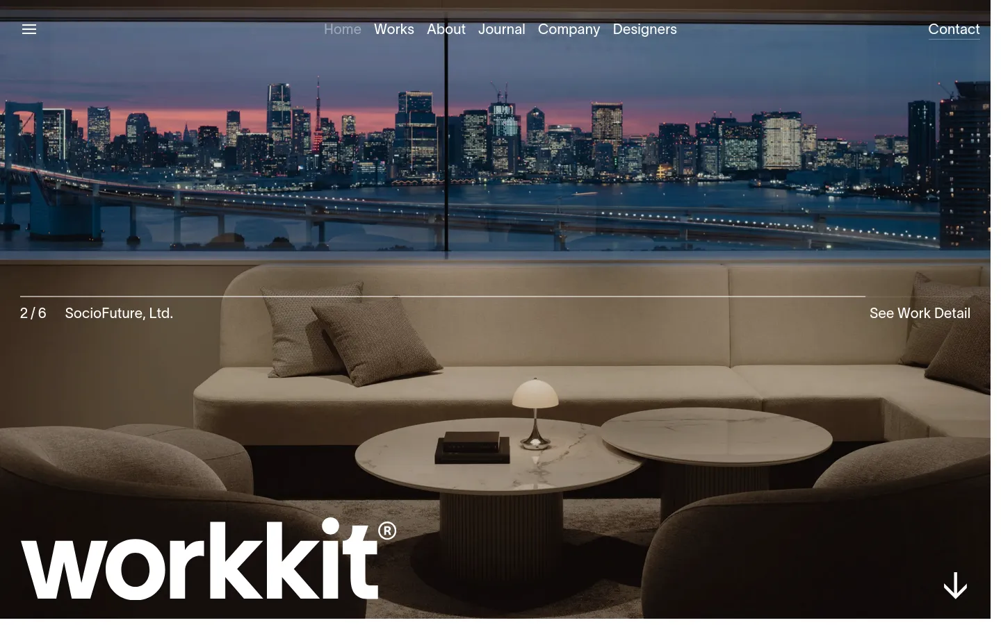 The desktop homepage features a large hero image of a modern lounge area with a city skyline view at dusk. The 'workkit' logo is prominent in the bottom left, and a navigation menu sits at the top with links for Home, Works, About, Journal, Company, Designers, and Contact. A large arrow at the bottom right suggests scrolling for more content.