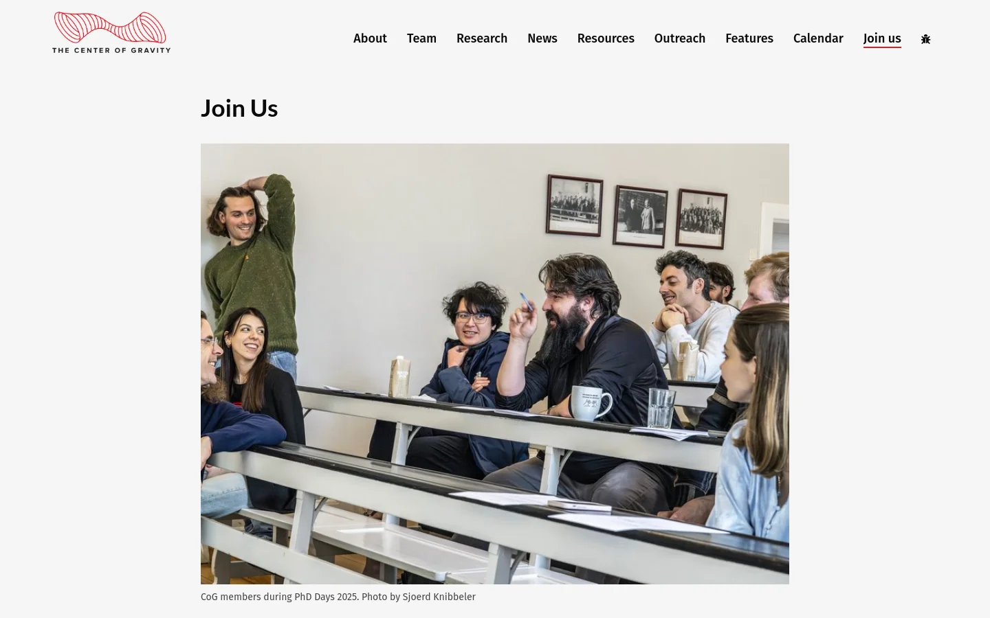 The desktop page features a white background with a navigation menu at the top right and a red wavy logo on the left. A large hero image shows a group of diverse researchers sitting at long white desks in a bright room, followed by the headline 'Join Us' and several paragraphs of text regarding student and visitor opportunities.